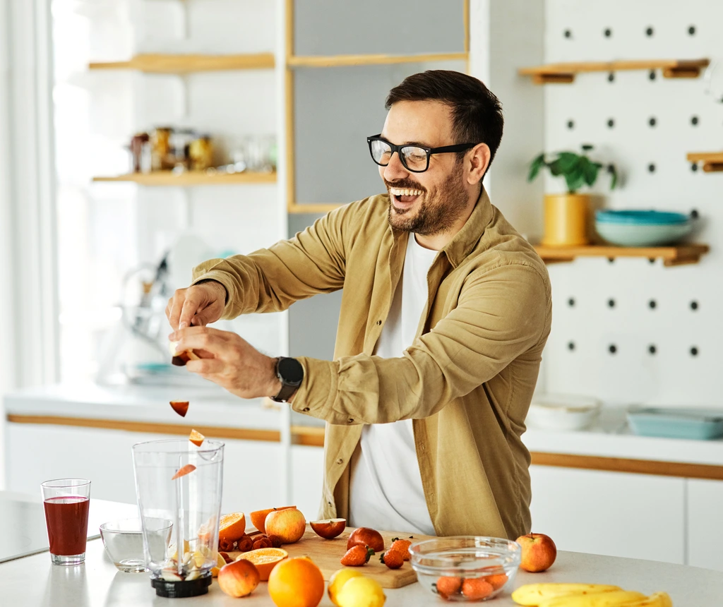 Ethan Carter laughing as he adds fresh fruit into a blender to make a smoothie recipe from Little Kitchen Diary.