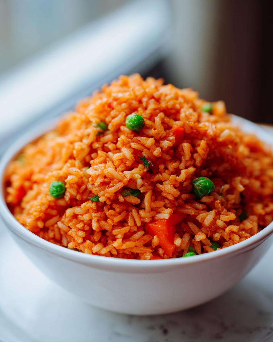 Close-up of fluffy, orange-colored spanish rice mixed with green peas and diced carrots in a white bowl.
