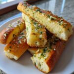 A stack of golden, fluffy breadsticks generously topped with melted garlic butter and fresh parsley.