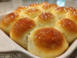 Close-up of freshly baked, soft dinner rolls with a shiny, buttery glaze in a white baking dish.