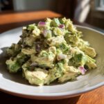 A mound of creamy avocado chicken salad featuring chunks of chicken, green avocado, and diced red onion served in a light-colored bowl.