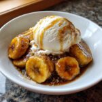 Close-up of warm, caramelized bananas in sauce topped with vanilla ice cream, a perfect serving of bananas foster.