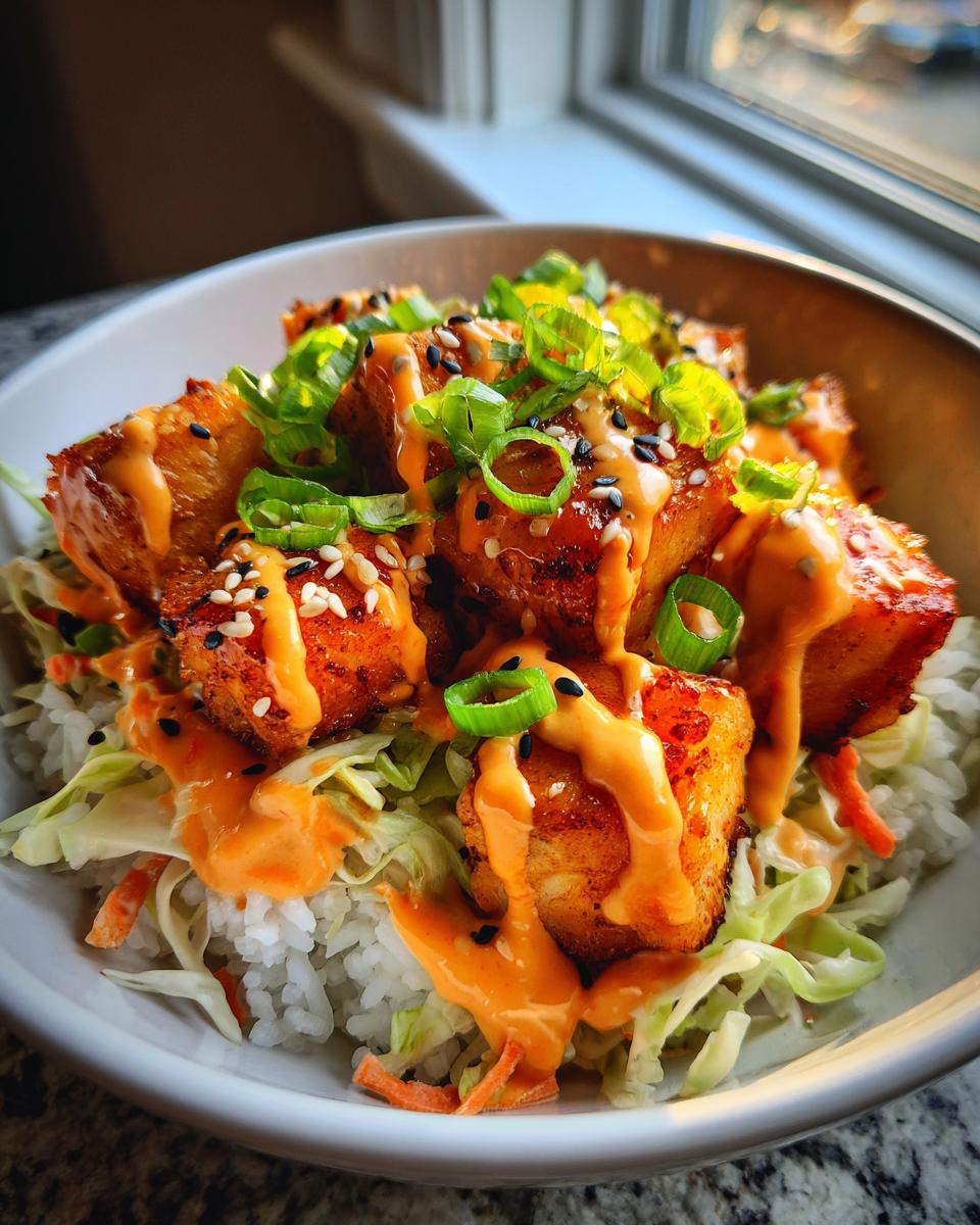 A close-up of a delicious Bang Bang Salmon Bowls featuring crispy salmon pieces over rice and slaw, drizzled with orange sauce and topped with green onions.
