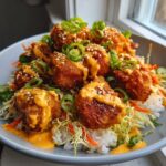 A close-up of a bowl filled with crispy, sauced Bang Bang salmon bites over rice and shredded vegetables.