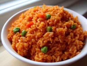 Close-up of a white bowl filled with fluffy, bright orange Spanish rice mixed with green peas and diced carrots.