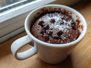 A freshly baked chocolate mug cake dusted with powdered sugar and topped with chocolate chips.