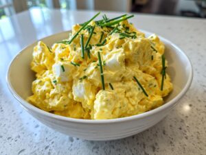 A close-up of a creamy, yellow classic egg salad recipe, topped generously with fresh green chives.