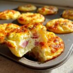A close-up view of a freshly baked cottage cheese egg cups starbucks recipe, showing one cup broken open to reveal a fluffy interior with pieces of ham.