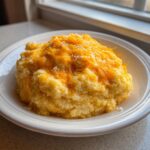 A close-up of a generous serving of creamy cheese grits topped with melted orange cheddar cheese.