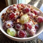 Close-up of creamy chicken salad chick grape salad featuring red and green grapes coated in dressing and topped with chopped pecans.