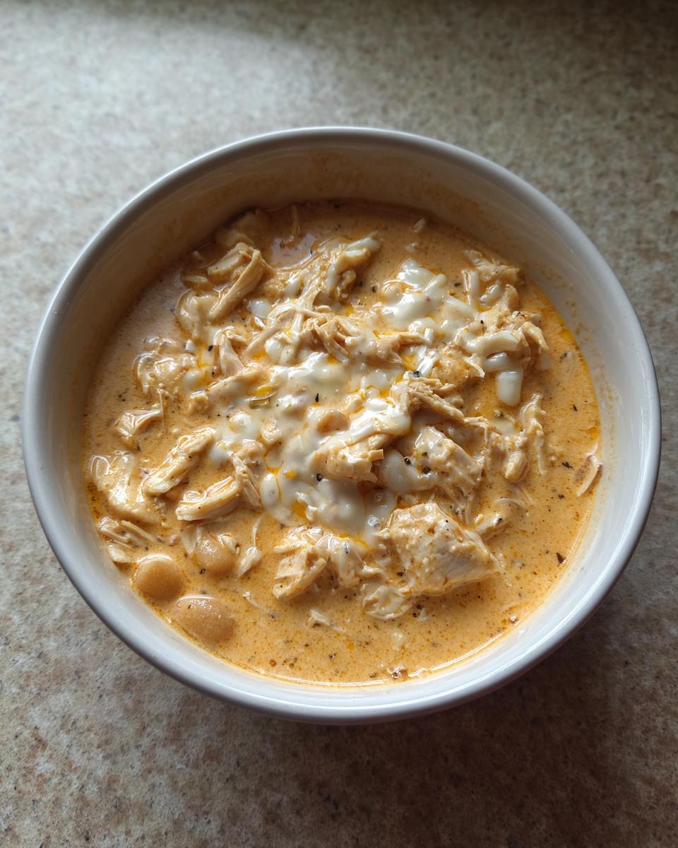 Overhead view of a bowl filled with creamy crockpot white chicken chili topped with melted cheese.
