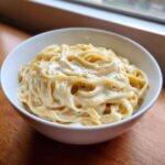 Close-up of fettuccine pasta generously coated in rich, creamy homemade alfredo sauce and topped with cracked black pepper.