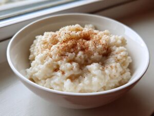 Close-up of creamy rice pudding in a white bowl, generously sprinkled with ground cinnamon.