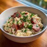 A close-up of a creamy sausage and rice skillet dish topped with sliced smoked sausage and fresh parsley.