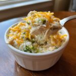 A spoonful of creamy crock pot chicken and rice mixed with broccoli and topped with melted cheddar cheese.