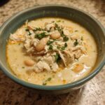 Close-up of a bowl of creamy crockpot white chicken chili topped with shredded chicken, white beans, and fresh parsley.
