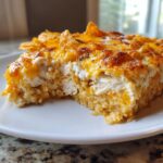 A close-up, tempting slice of Dorito Casserole showing layers of rice, shredded chicken, creamy sauce, and melted cheddar cheese topped with chips.