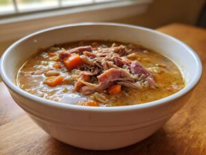 Close-up of a white bowl filled with rich Ham and bean soup, topped with shredded ham and carrots.