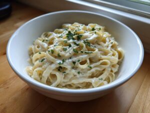 A white bowl filled with fettuccine pasta coated in rich homemade alfredo sauce and topped with fresh parsley.