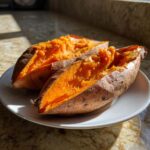 Two halves of a fluffy baked sweet potato showing bright orange flesh served on a white plate.