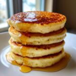 A tall stack of four fluffy sourdough pancakes drizzled generously with golden syrup.