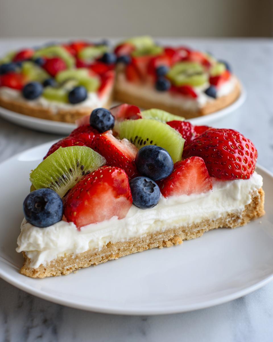 A close-up slice of fruit pizza sugar cookie topped with cream cheese frosting, strawberries, blueberries, and kiwi.