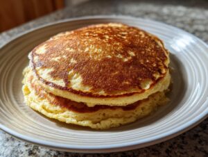 A close-up of two fluffy almond flour pancakes stacked on a light brown plate.