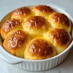 Close-up of six golden brown, soft dinner rolls baked together and generously brushed with a shiny honey or butter glaze.