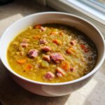 Close-up of a hearty bowl of thick pea soup topped with diced ham and carrots.