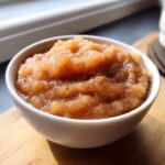 A close-up of a white bowl filled with chunky, homemade applesauce, lightly dusted with cinnamon.