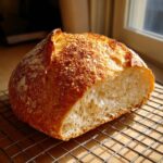 A freshly baked loaf of Italian bread, cut to show the airy interior, resting on a cooling rack.