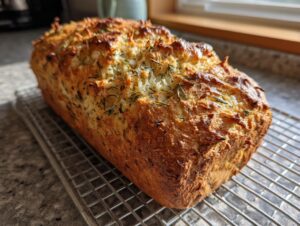 A freshly baked loaf of Italian herb and cheese bread with a golden, craggy top, cooling on a wire rack.