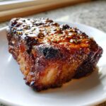 Close-up of a thick, juicy pork steak recipe cut, covered in a dark, glossy glaze with visible herbs and spices.