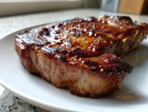 Close-up of a perfectly cooked, glazed pork steak resting on a white plate, showing a caramelized crust.