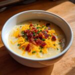 A creamy bowl of Loaded Baked Potato Soup topped generously with shredded cheddar cheese, crispy bacon bits, and fresh chives.