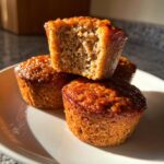 Close-up of three moist honey bran muffins stacked, with the top one broken open to show the texture.