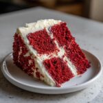 A close-up of a perfectly moist slice of red velvet cake layered with thick cream cheese frosting.