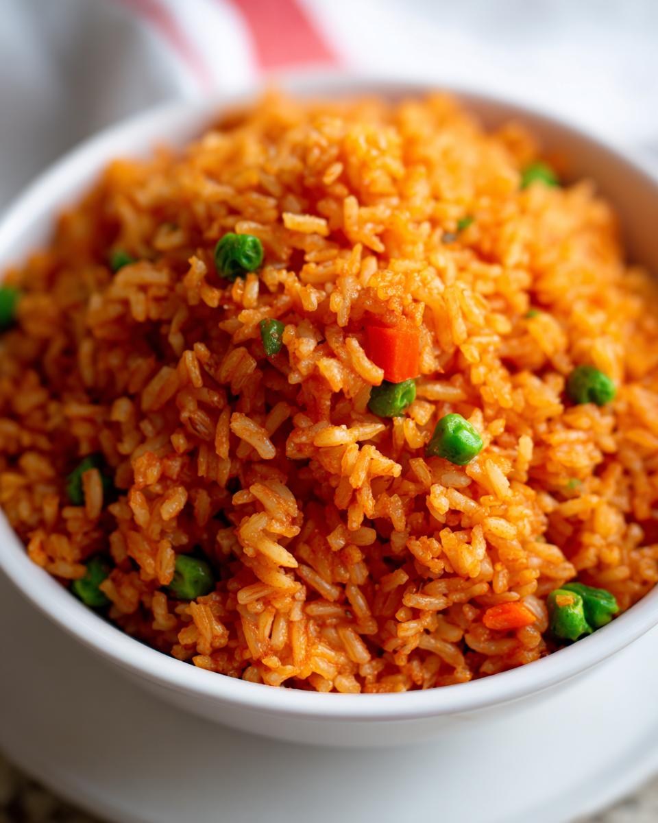Close-up of fluffy, bright orange Spanish rice mixed with green peas and diced carrots, served in a white bowl.