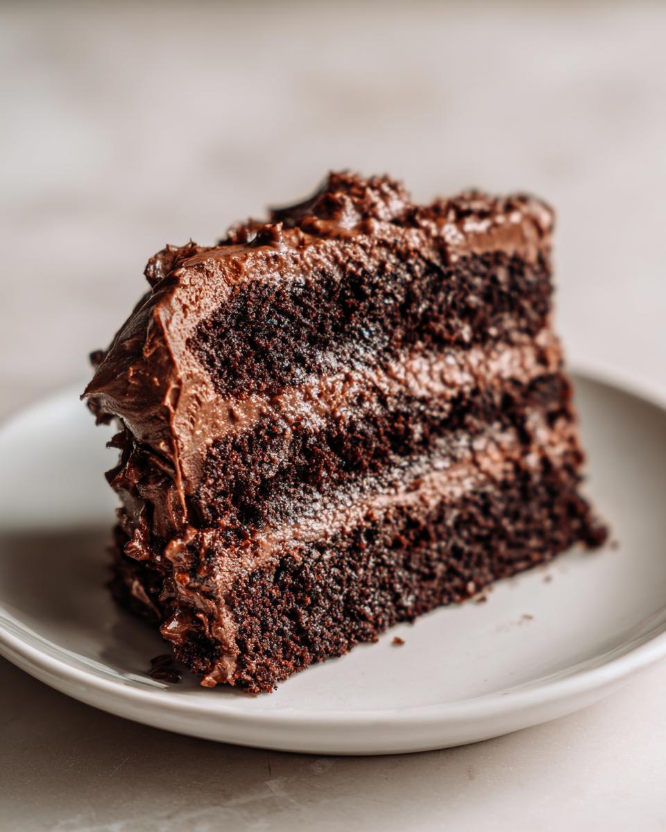 Close-up of a moist, three-layer slice of German chocolate cake recipe with thick chocolate frosting.