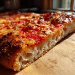 Close-up of a thick slice of pizza showing the airy, open crumb structure made from sourdough discard pizza dough.