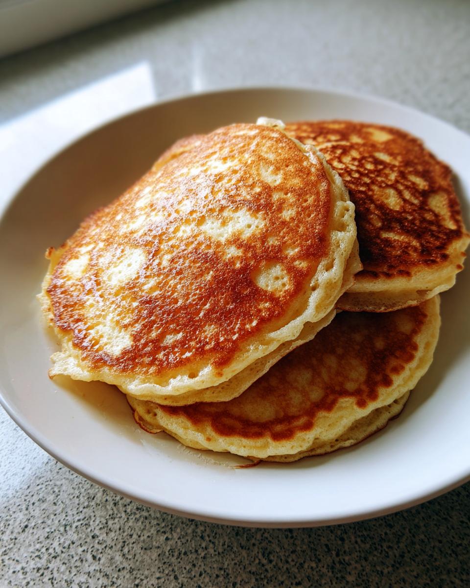 A stack of three perfectly golden brown almond flour pancakes served on a white plate.