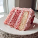 A tall slice of layered strawberry cake with pink frosting and a fresh strawberry garnish.