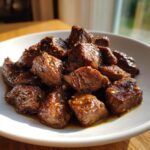 Close-up of tender, cubed crockpot steak pieces coated in a rich, glossy brown sauce with visible garlic bits.