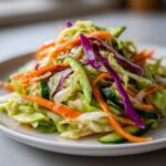 A close-up of a fresh, colorful cabbage salad featuring shredded green cabbage, purple cabbage, carrots, and cucumber slices.