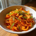 Close-up of a vibrant raw carrot salad made with shaved carrot ribbons, coated in dressing, and topped with green onions and black sesame seeds.