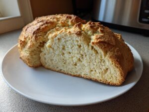 A loaf of golden brown soda bread cut in half, revealing a soft, airy interior texture.