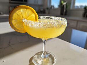 A bright yellow lemon drop cocktail in a coupe glass with a thick sugar rim and a fresh lemon slice garnish.