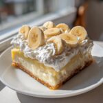 A decadent square slice of banana cream pie topped with whipped cream and fresh banana slices.