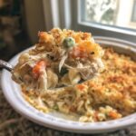 A spoonful of creamy chicken noodle casserole, showing shredded chicken, peas, carrots, and a crunchy breadcrumb topping.