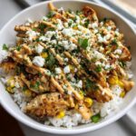 Close-up of a delicious chicken rice bowl featuring grilled chicken, corn, crumbled white cheese, and a creamy sauce drizzle.